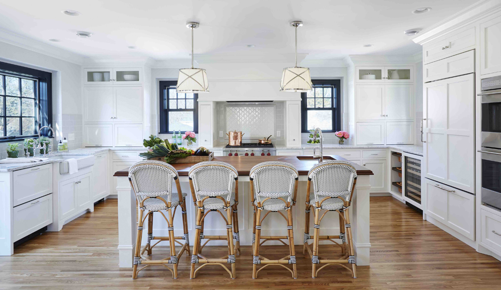 White kitchen with rattan kitchen stools. Kitchen with drum pendant lights over white kitchen island with wooden countertop 