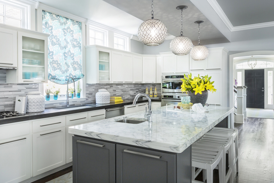 White kitchen with gray marble mosaic tile backsplash. Kitchen with globe pendant lights over grey kitchen island with marble countertop