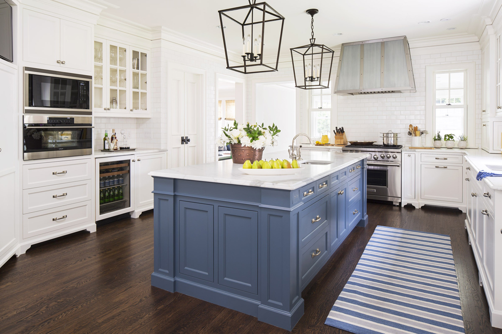 White kitchen with dark wood floors. Kitchen with box pendant lights over blue kitchen island with white marble countertop