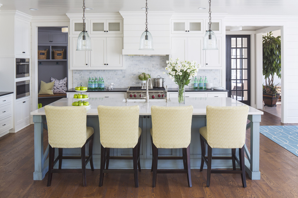 White kitchen with cream leather bar stools. Kitchen with glass pendant lights over blue kitchen island with white countertop