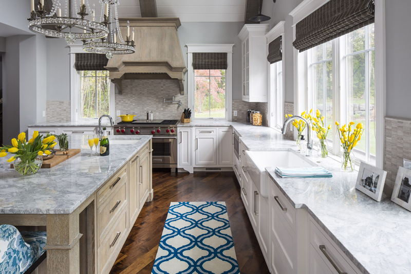 White kitchen with maple floors. Kitchen with candle chandelier over wood kitchen island with marble countertop 