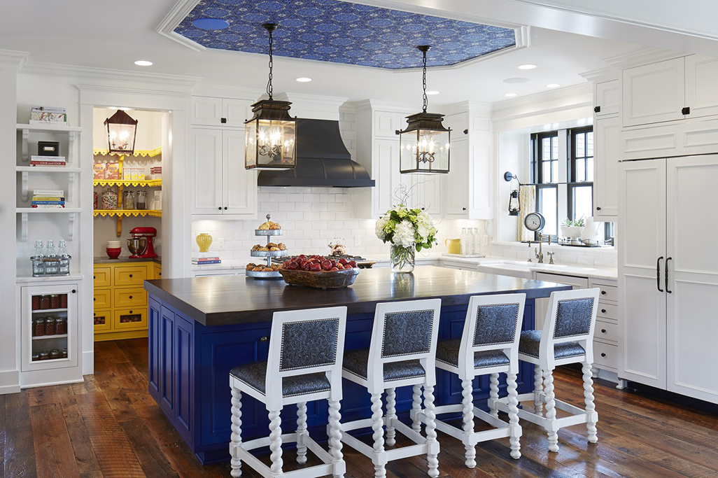 White kitchen with white bar stools and reclaimed oak flooring. Kitchen with lantern pendant lights over navy kitchen island with dark wood countertop