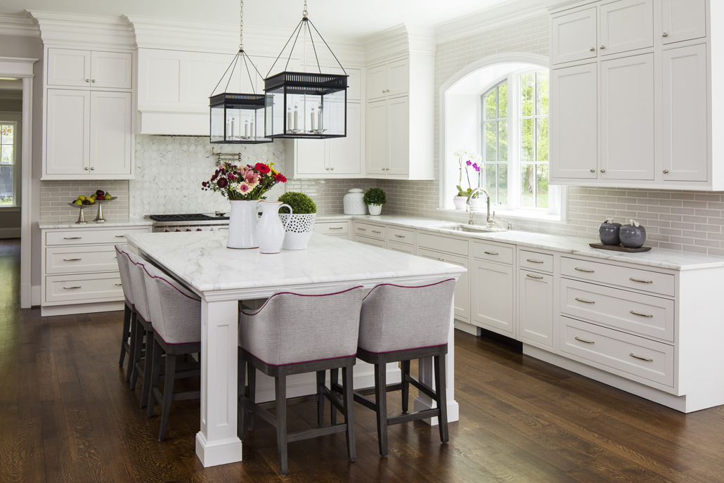 White kitchen with gray tiled backsplash with dark wood floors. Kitchen with lantern pendant lights over white kitchen island with white countertop 