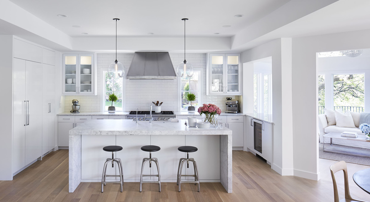 White kitchen with dark laminate wood floor texture. Kitchen with bar stools with glass pendant lights over white kitchen island with white marble countertop