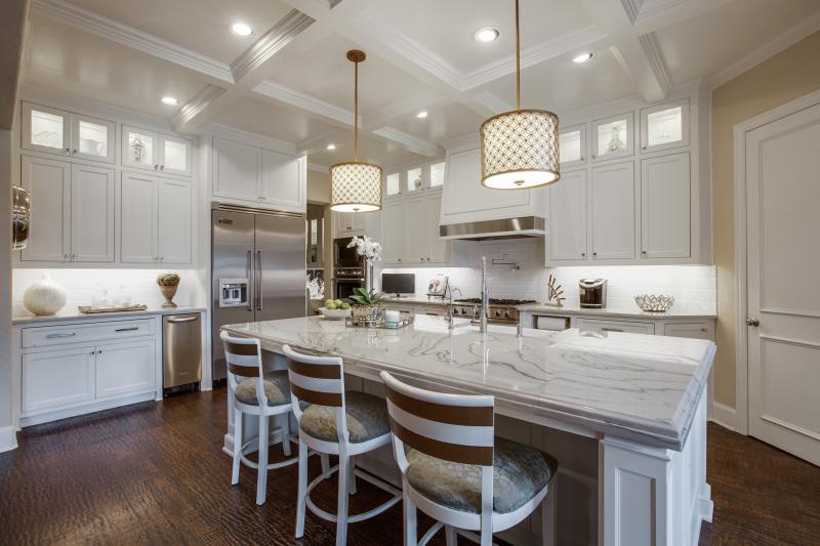 White kitchen with white brown bar stools and dark wood floors. Kitchen with drum shade pendant lights over white kitchen island with marble countertops