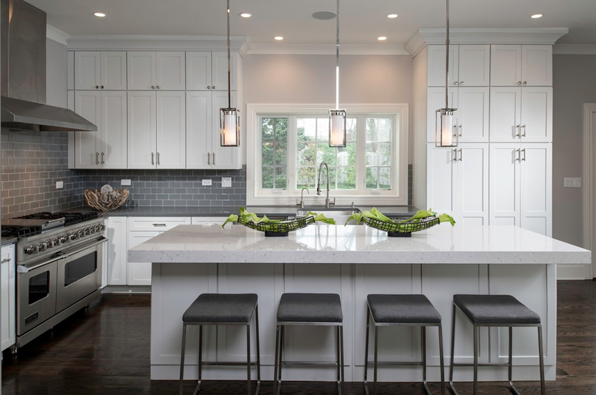 White kitchen with gray upholstered bar stools and gray backsplash. Kitchen with tube pendant lights over white kitchen island with laminate countertop