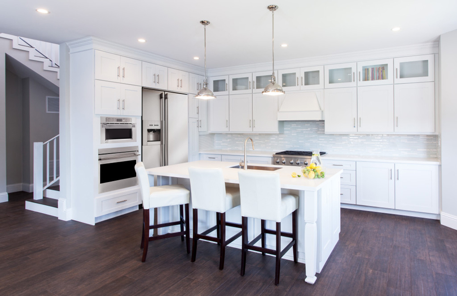 White kitchen with gray mosaic tile backsplash, white bar stools and dark wood floors 