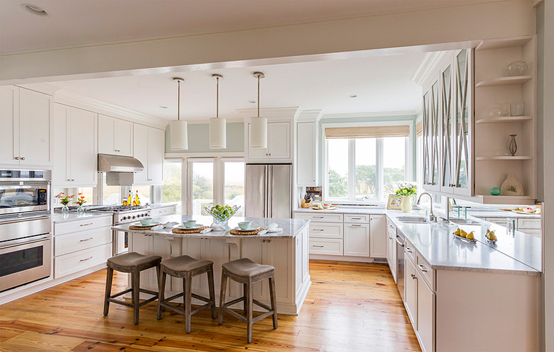 White kitchen with saddle bar stools and light wood floors. Kitchen with tube pendant lights over white kitchen island with marble countertops