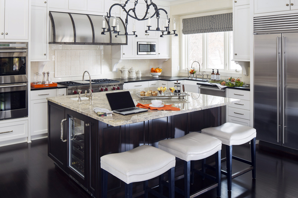 White kitchen with light dark hardwood floors. Kitchen with bar stools with candle pendant light over dark brown kitchen island with marble countertop