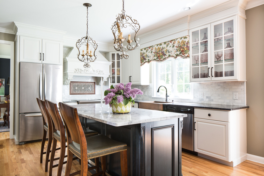 Small white kitchen with wooden bar stools and black kitchen island. Kitchen with arcadia chandeliers over black kitchen island with marble countertop
