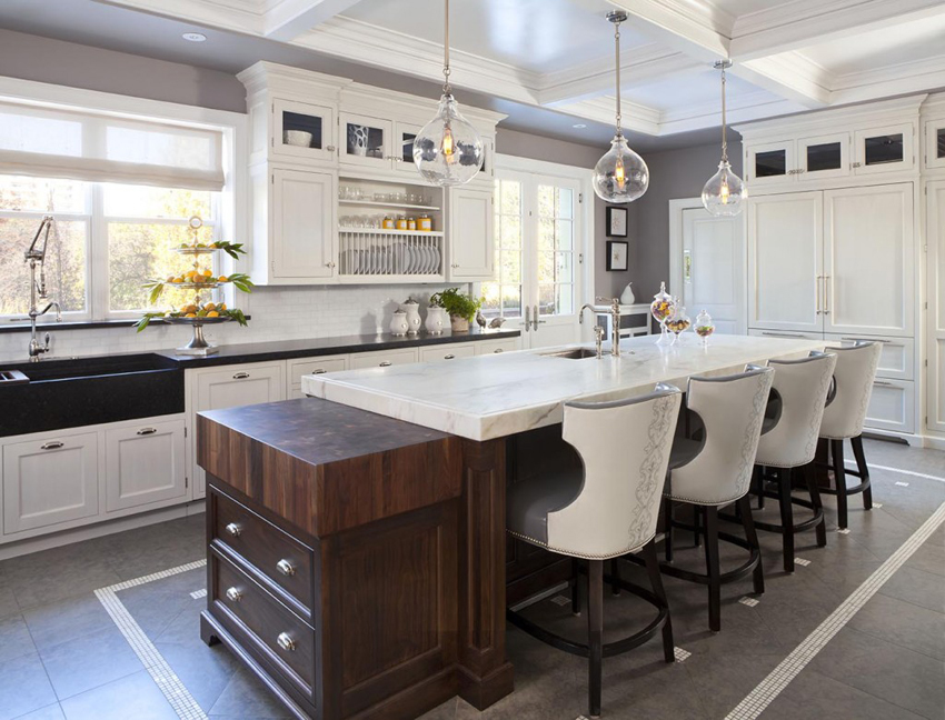 White kitchen with gray tile floors and white bar stools. Kitchen with glass pendant lights over wooden kitchen island with marble countertop