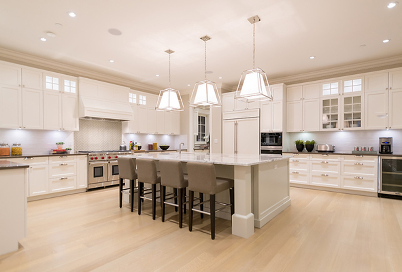 White kitchen with grey bar stools. Kitchen with white pendant lights over white kitchen island with marble countertops