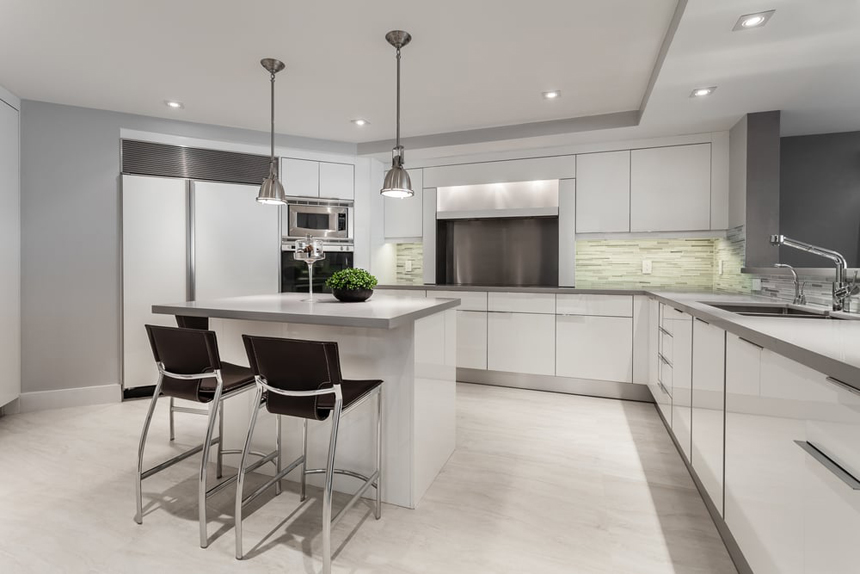 Modern white kitchen with brown leather bar stools. Kitchen with chrome pendant lights over white kitchen island with laminate countertops
