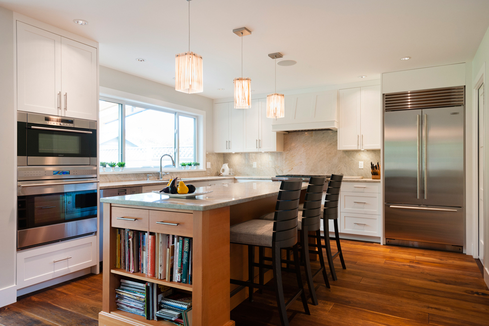 White kitchen with stainless appliances. Kitchen with bar stools with white square pendant lamp over wooden kitchen island with gray marble countertop