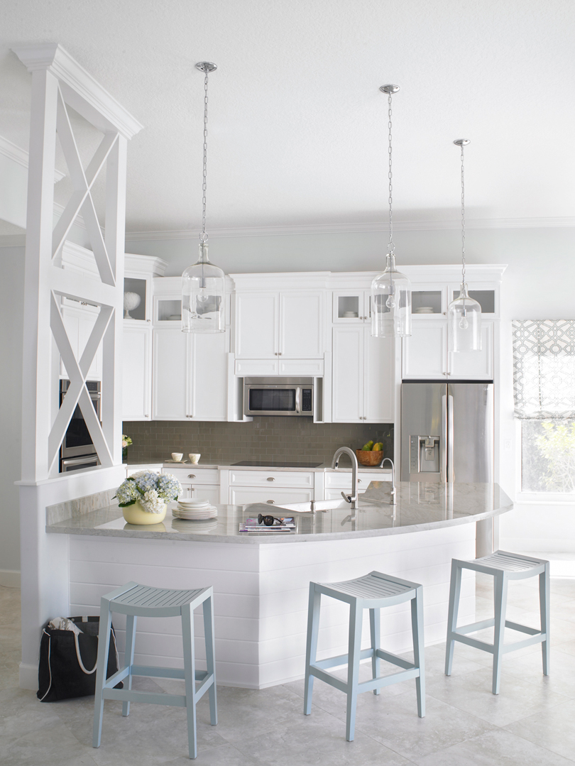 White kitchen with grey tile backsplash, saddle bar stools and glass pendant lights