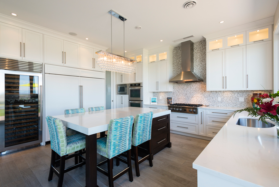 White kitchen with blue accents. Kitchen with linear crystal chandelier over dark kitchen island with white laminate countertop