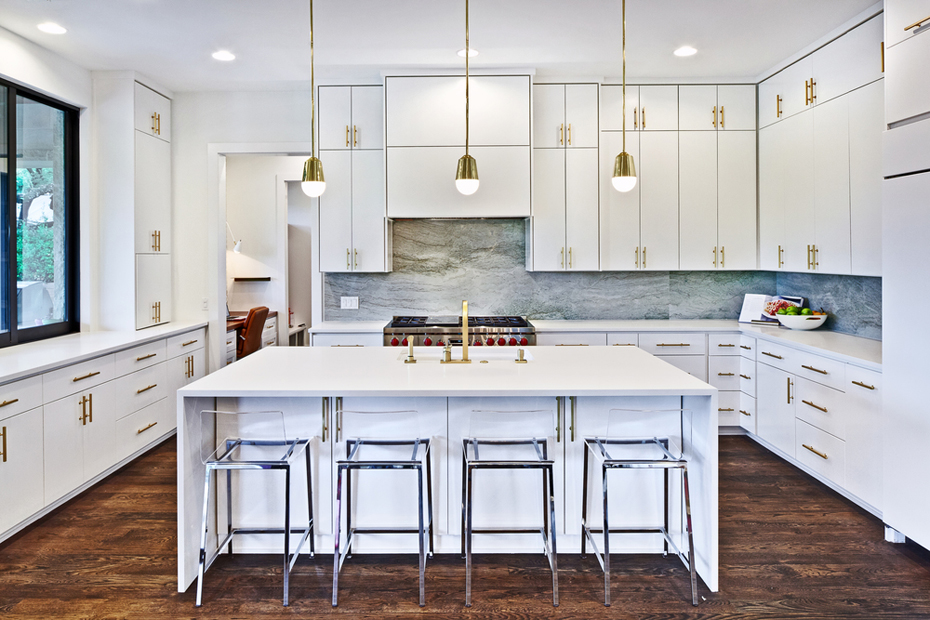 White kitchen with marble tile backsplash and glass bar stools. Kitchen with mini gold pendant lights over white kitchen island with laminate countertops