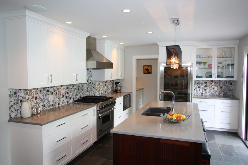 White kitchen with gray tile flooring. Kitchen with linear crystal chandelier over wooden kitchen island with white laminate countertop