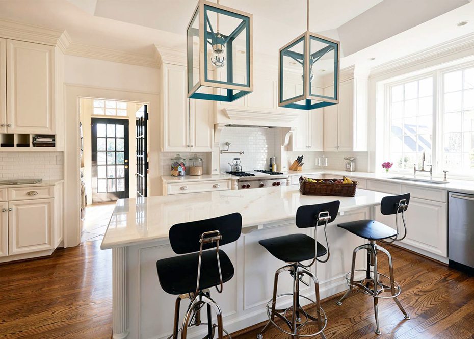 White kitchen with modern black upholstered bar stools and white kitchen island. Kitchen with blue box pendant lights over white kitchen island with marble countertops