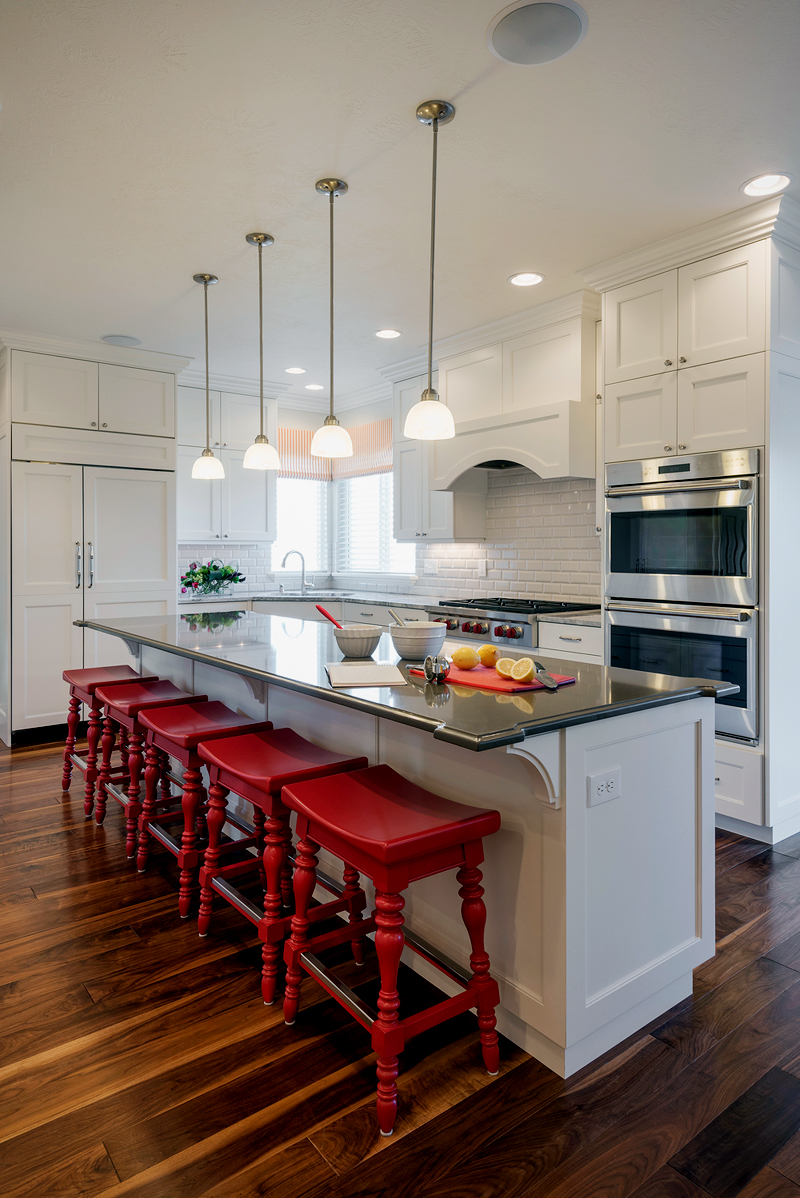 Wite kitchen with red saddle bar stools. Kitchen with mini pendant lights over white kitchen island with black countertops