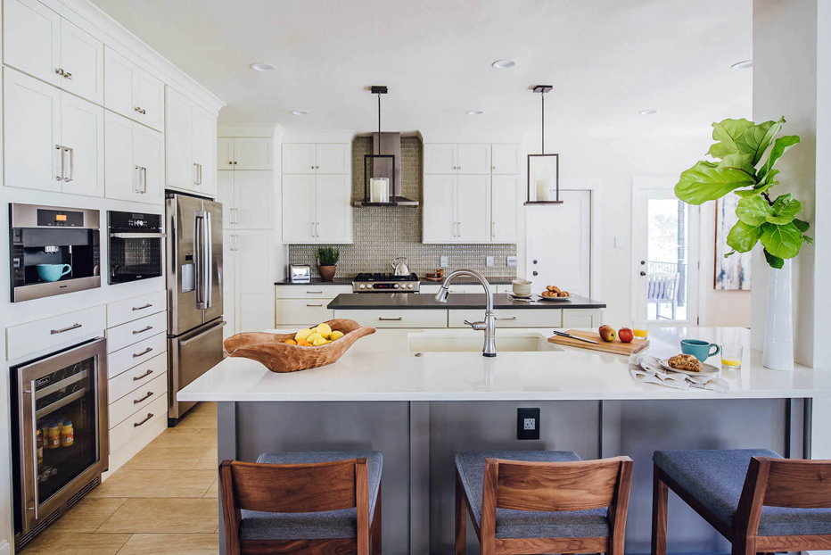 White kitchen with with white cabinets and bar stools. Kitchen with candle pendant lights over wooden kitchen island with black laminate countertop