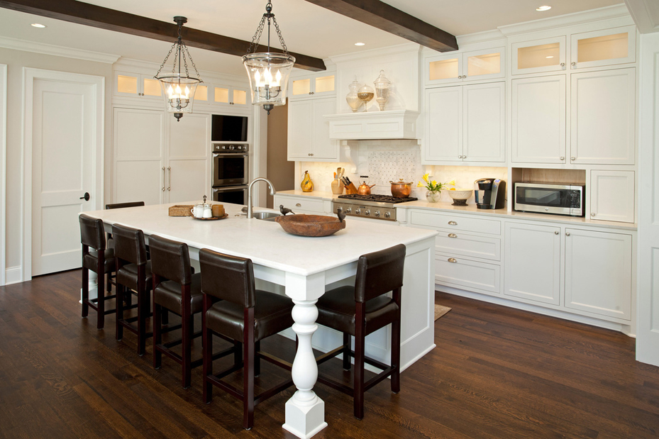White kitchen with brown leather bar stools and dark wood floors. Kitchen with lantern glass pendant light over white kitchen island with laminate countertop
