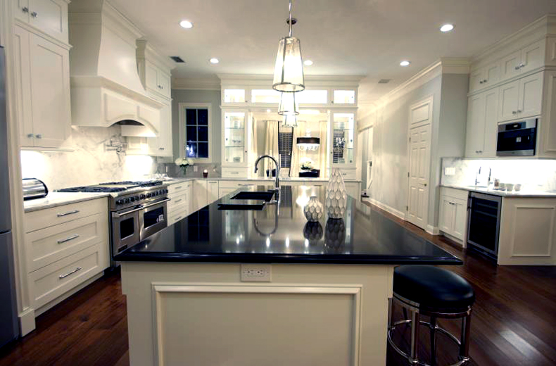 White kitchen with glass tube pendant lamp over white kitchen island with black quartz countertop
