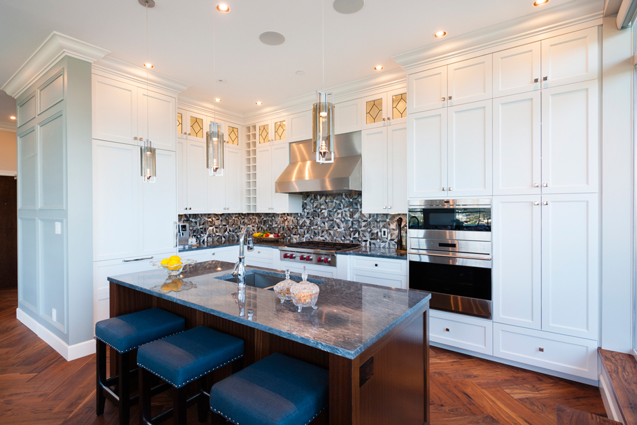 White kitchen with navy bar stools and gray backsplash. Kitchen with tube pendant lights over wood kitchen island with marble countertop