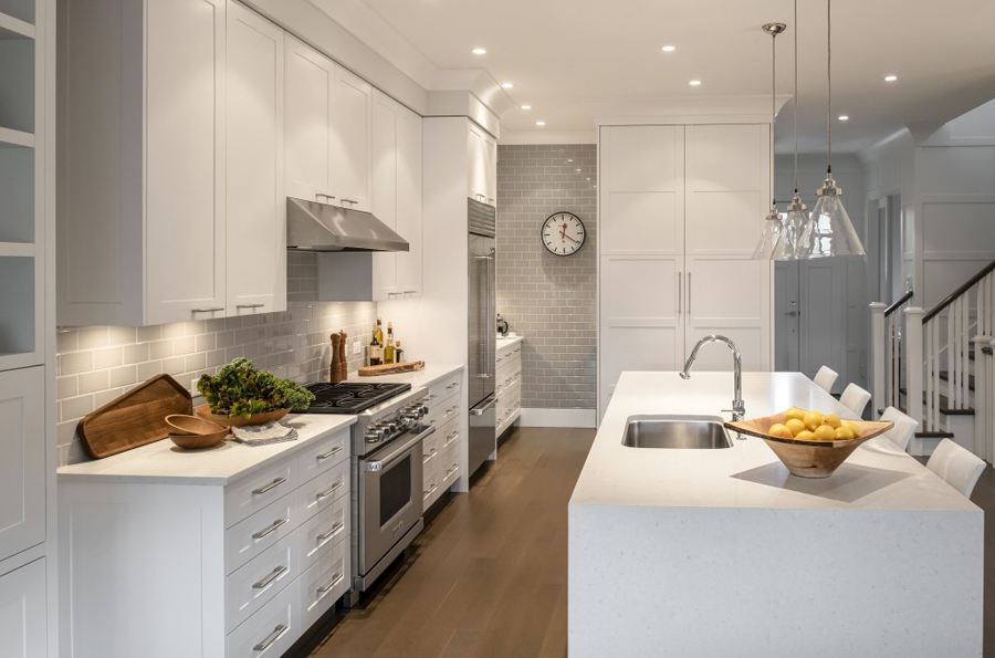 Wite kitchen with gray subway tile backsplash. Kitchen with glass pendant lights over white kitchen island