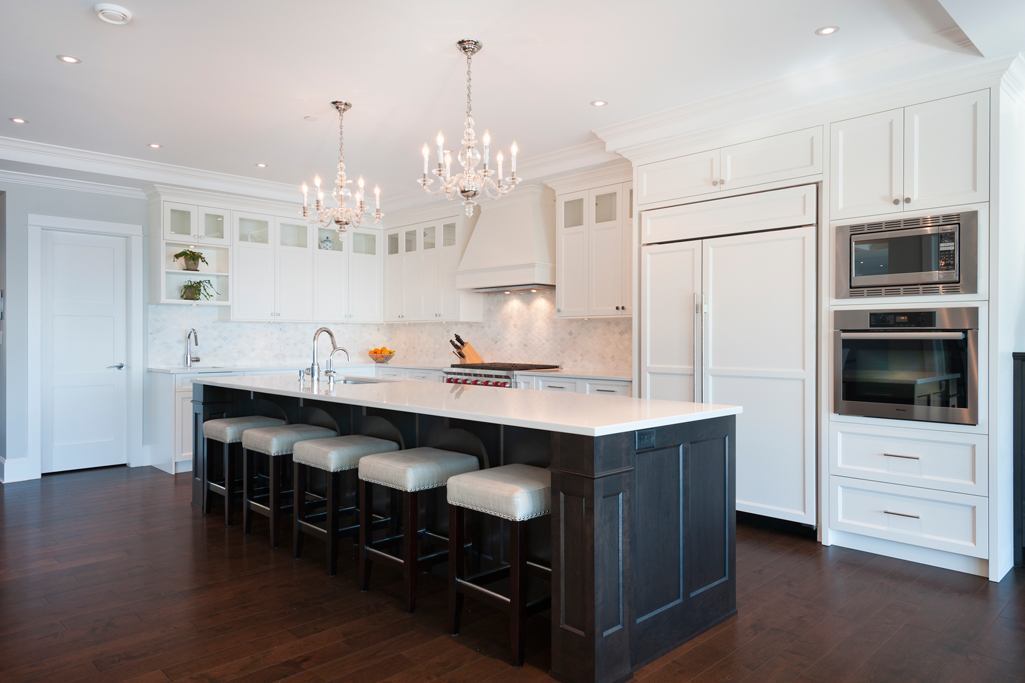 White kitchen with white backsplash and dark wood floors. Kitchen with mini candle chandelier over black kitchen island with white laminate countertop