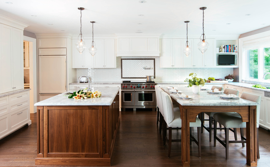 White kitchen with dining table in the middle. Kitchen with clear glass pendant lights over wooden kitchen island with marble countertop