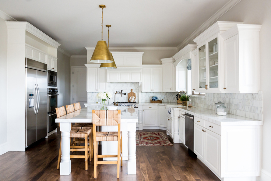 White kitchen with wooden bar stools and dark wood floors. Kitchen with gold pendant lights over kitchen island with white laminate countertop