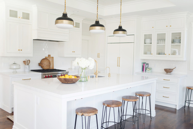 White kitchen with wood and iron bar stools. Kitchen with black gold pendant lights over white kitchen island with marble countertop