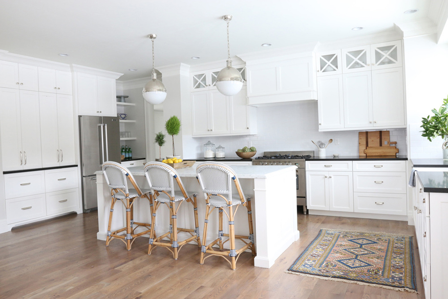 White kitchen with rattan bar stools and hardwood floors. Kitchen with white globe pendant lights over kitchen island with white laminate countertop