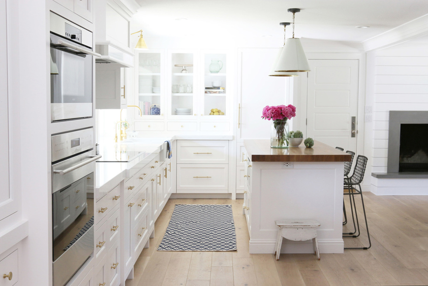 White kitchen with light oak wood flooring. Kitchen with white dome pendant lights over kitchen island with wooden countertops