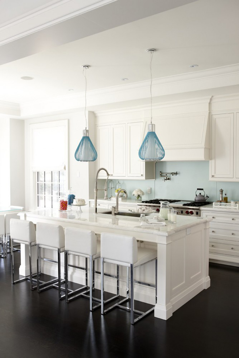 White kitchen with dark wood floors and blue backsplash. Kitchen with blue pendant lights over white kitchen island with marble countertops