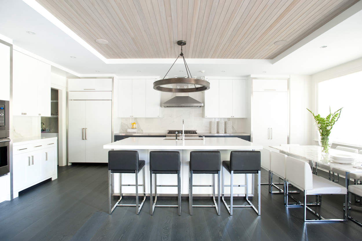 White kitchen with dark oak wood floors. Kitchen with round chandelier over white kitchen island with laminate countertops 
