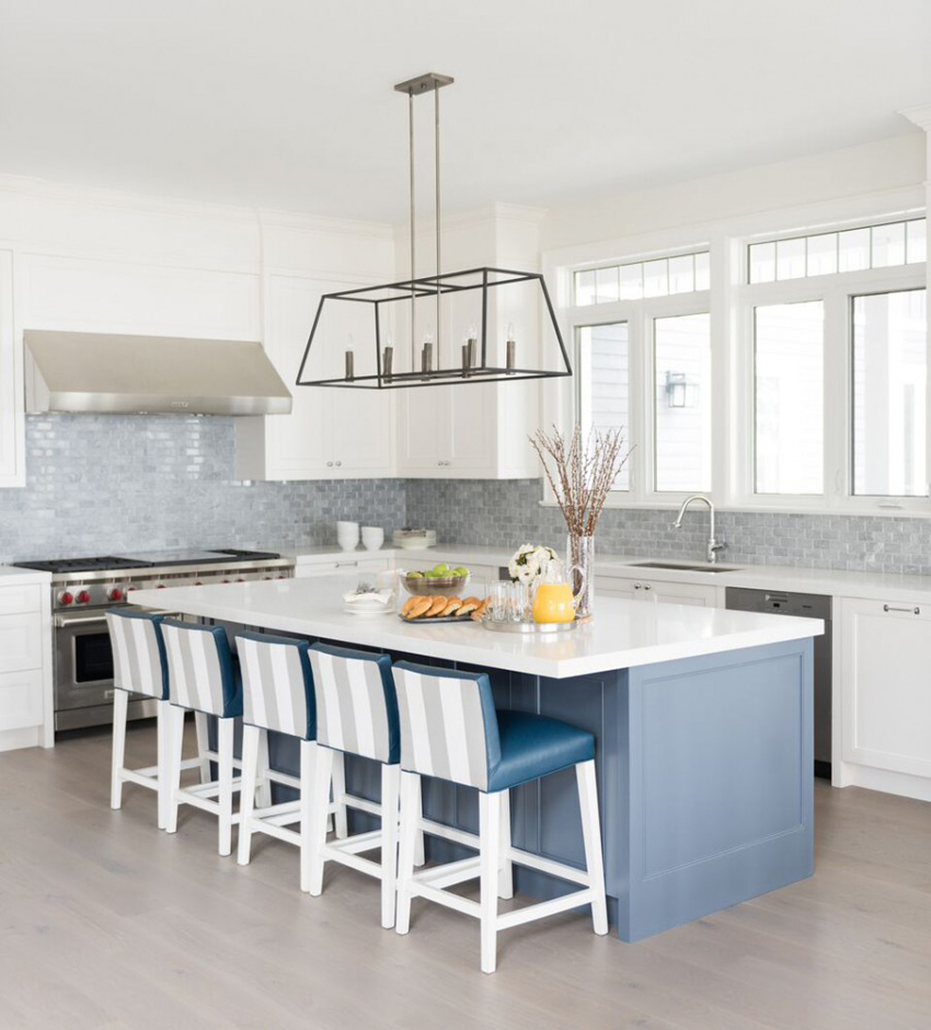 White kitchen with gray glass tile backsplash. Kitchen with box cage pendant lights over blue kitchen island with white laminate countertop