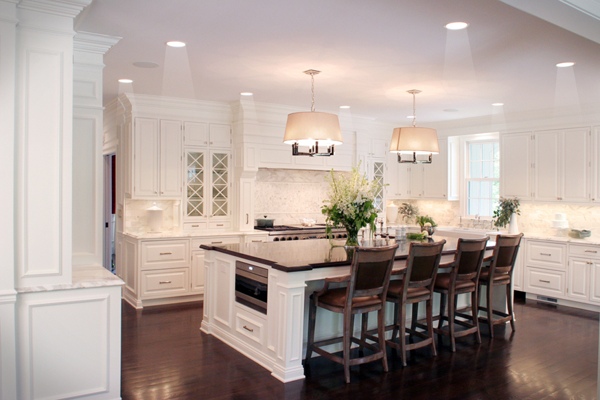 White kitchen with glossy solid dark hardwood floors. Kitchen with drum shade chandeliers over white kitchen island with dark chocolate countertop