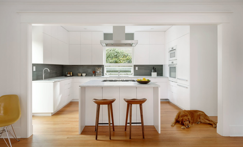 Modern white kitchen with wooden bar stools. Kitchen with gray backsplash , white kitchen island and light wood flooring