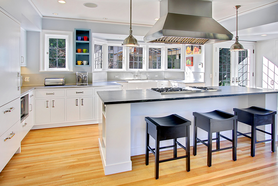 White kitchen with black wooden bar stools and light wood flooring. Kitchen with modern pendant lights over white kitchen island with black laminate countertop