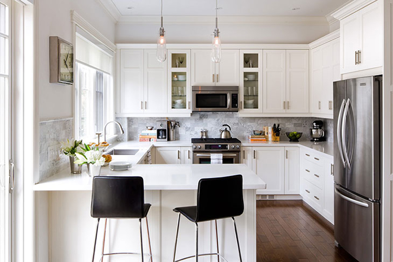 Small white kitchen with gray backsplash and black bar stools. Kitchen with glass tube pendant lights