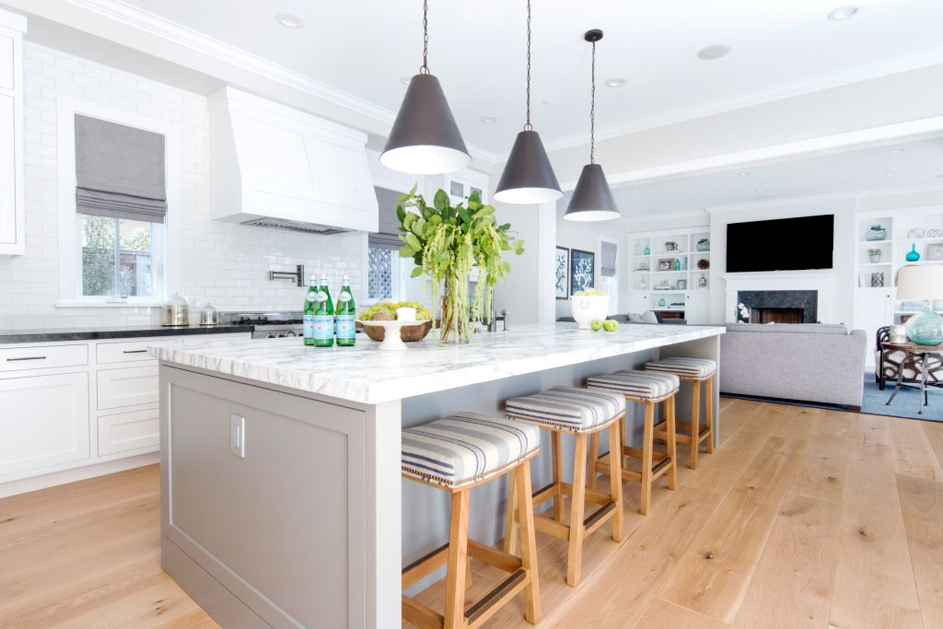 White kitchen with white tile backsplash and backless bar stools. Kitchen with contemporary pendant lights over gray kitchen island with marble countertop