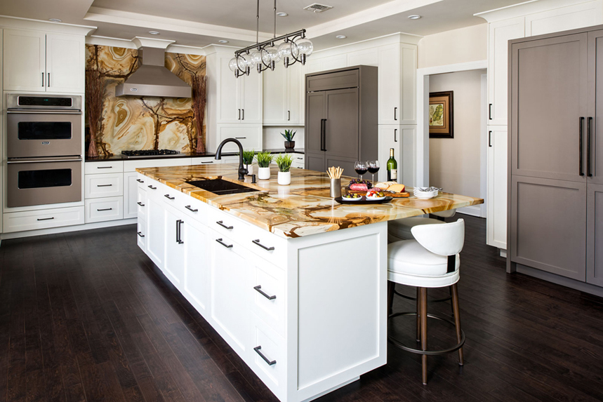 White kitchen with wood stone granite backsplash. Kitchen with track pendant lights over white kitchen island with stone wood granite countertop