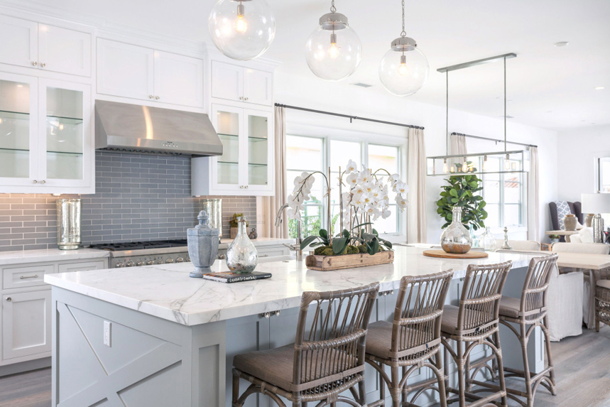 White kitchen with rattan swivel bar stools. Kitchen with glass ball pendant lights over gray kitchen island with marble countertop