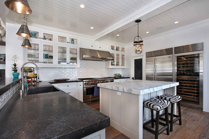 White kitchen with black quartz countertops. Kitchen with glass pendant lights over kitchen island with marble countertops