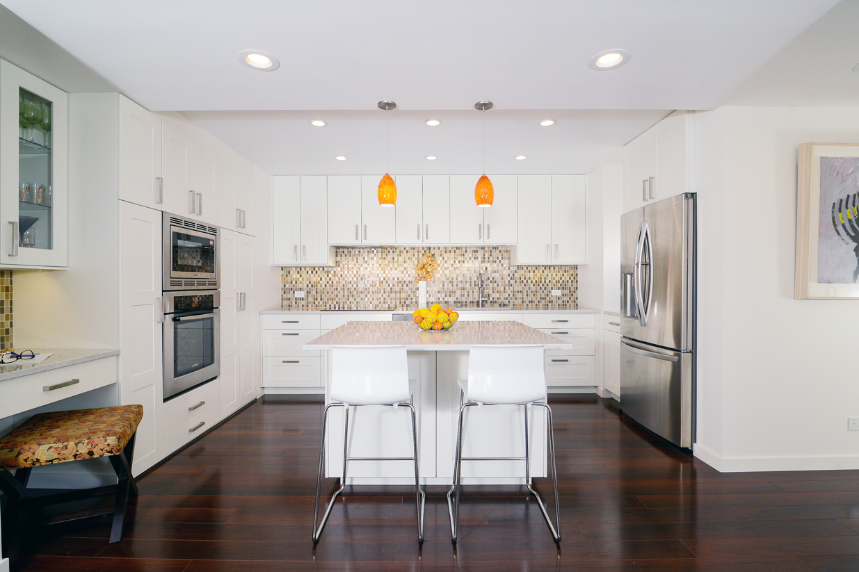 White kitchen cabinets with dark hardwood floors. White kitchen with orange pendant lights over kitchen island with marble countertops