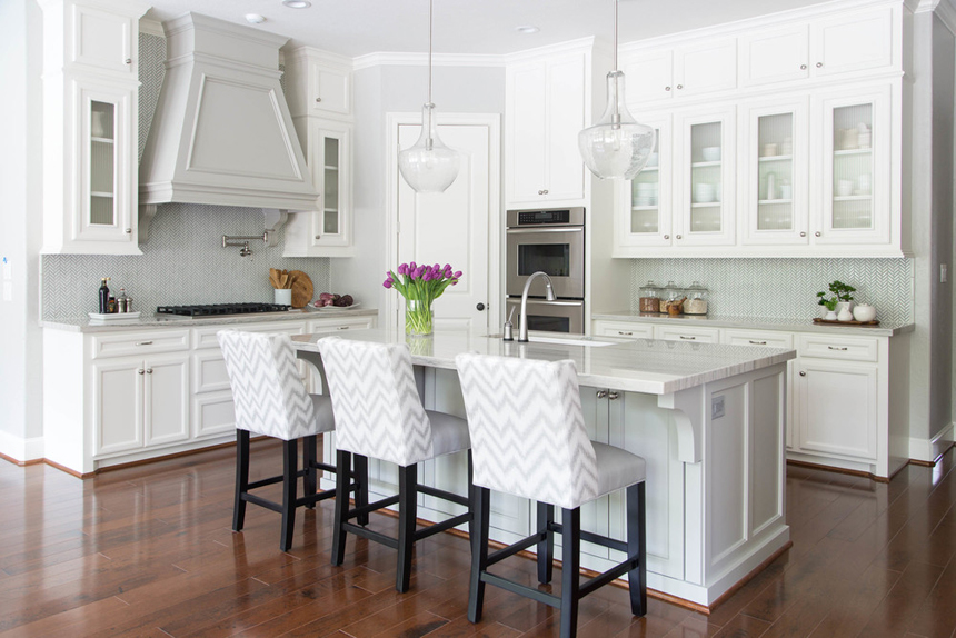 White kitchen black and white bar stools and hardwood floors. Kitchen with glass pendant lights over white kitchen island with marble countertops