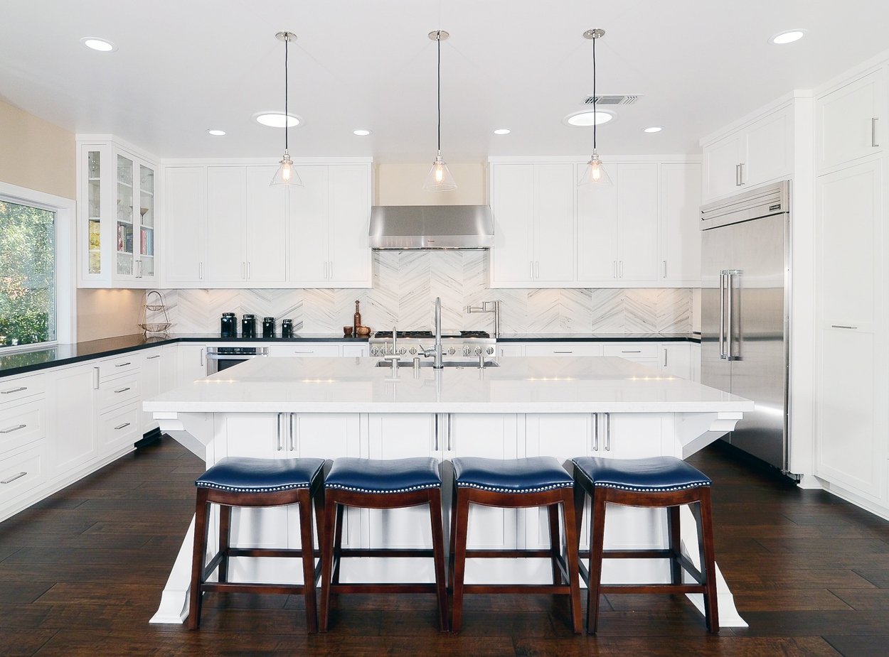 White kitchen with blue leather bar stools and hardwood floors. Kitchen with mini pendant lights over large kitchen island with white countertop