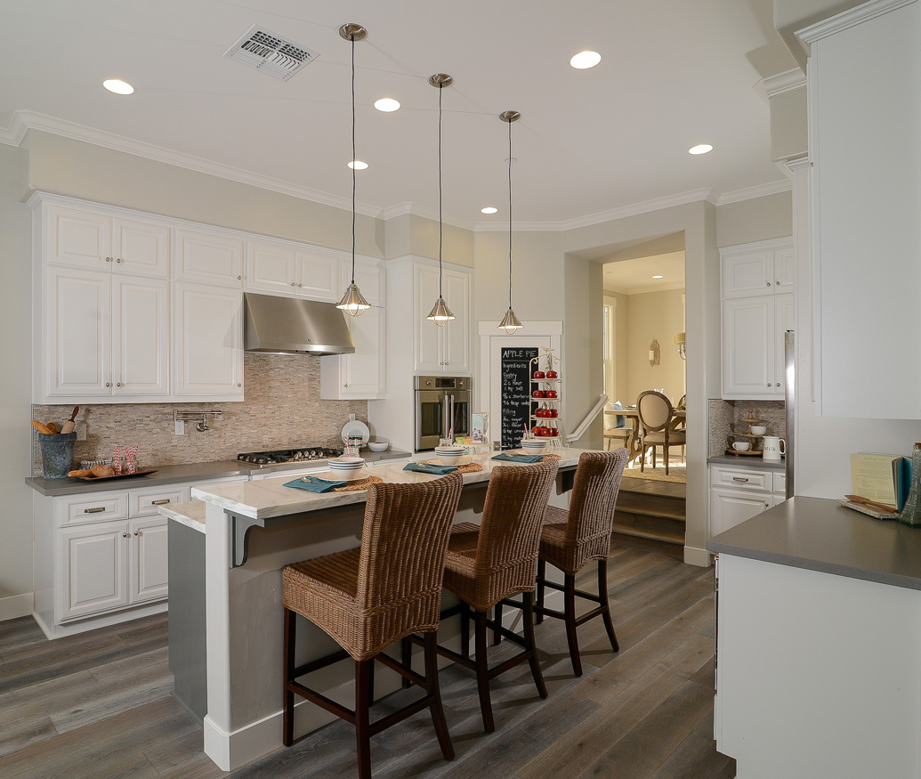 White kitchen with rattan wicker barstool. Kitchen with mini pendant lights over kitchen island with marble countertop